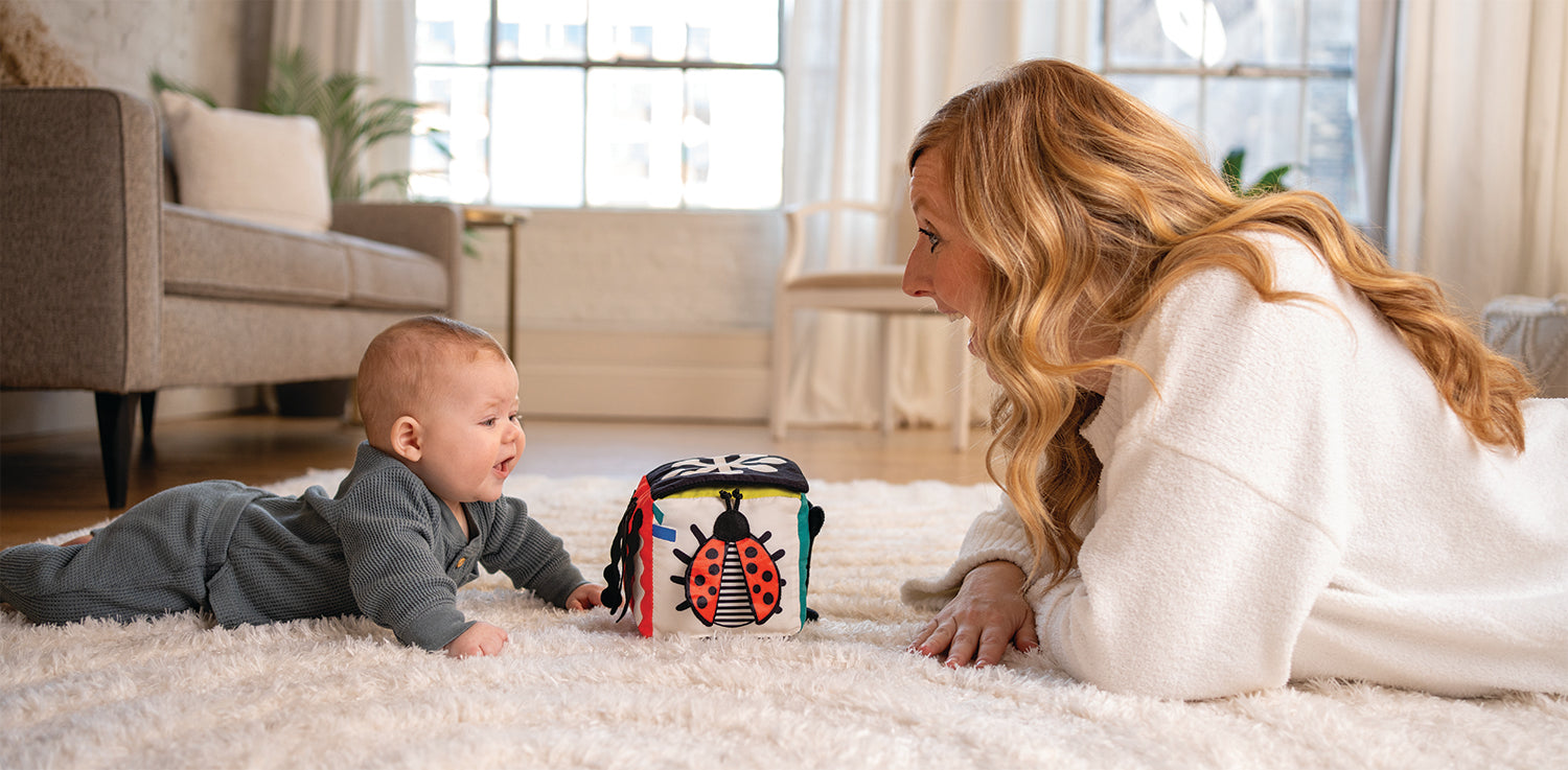 Mom and baby smiling and looking at one another while playing with an activity cube toy