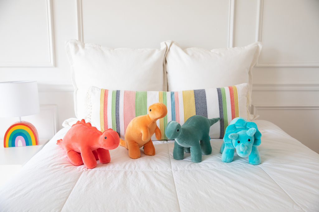 Stuffed animal dinosaurs on bed in room scene.